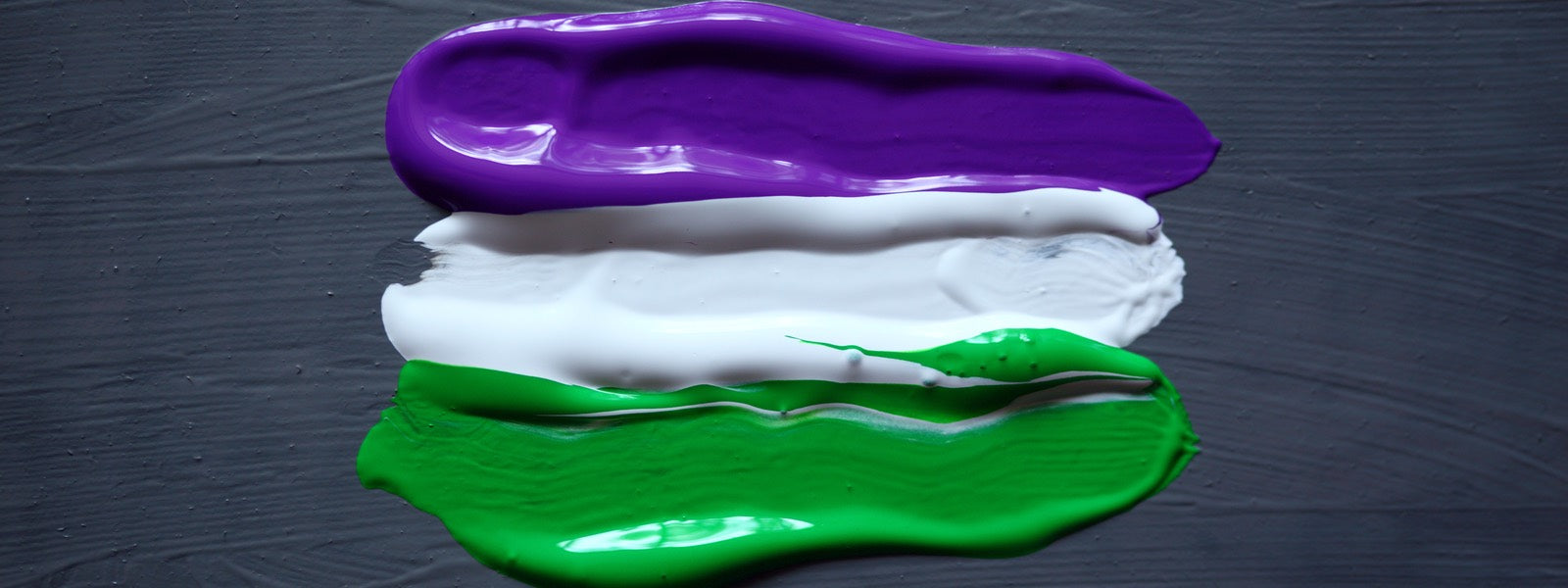 Three smears of acrylic paint in purple, white and green, mimicking the Genderqueer pride flag