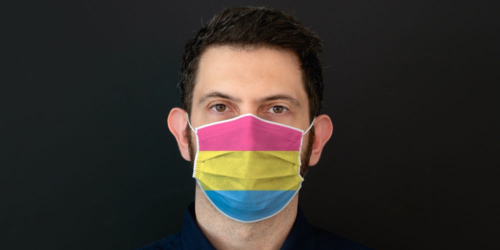 A man wearing a medical face mask in the colours of the pansexual pride flag: pink, yellow and blue