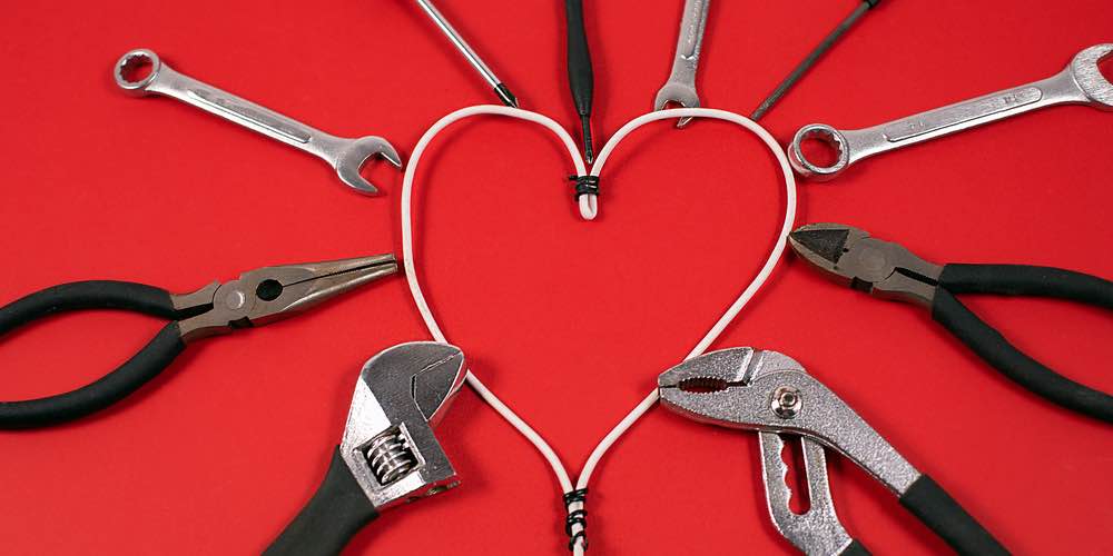 A picture of tools surrounding wire shaped into a heart on a red background