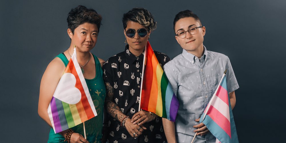 Three people holding rainbow and trans flags