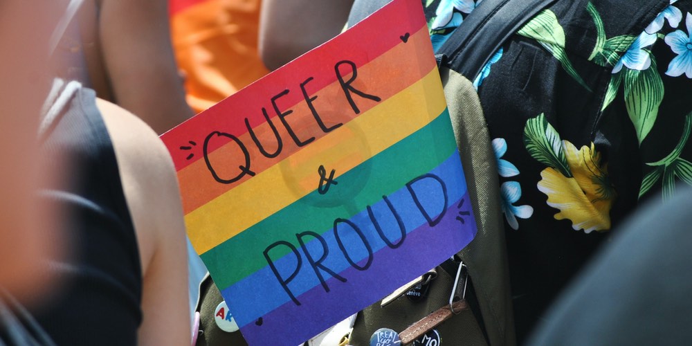 "Queer & Proud" written on a rainbow coloured placard